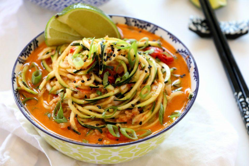Hands tossing zucchini noodles in coconut curry sauce in a skillet
