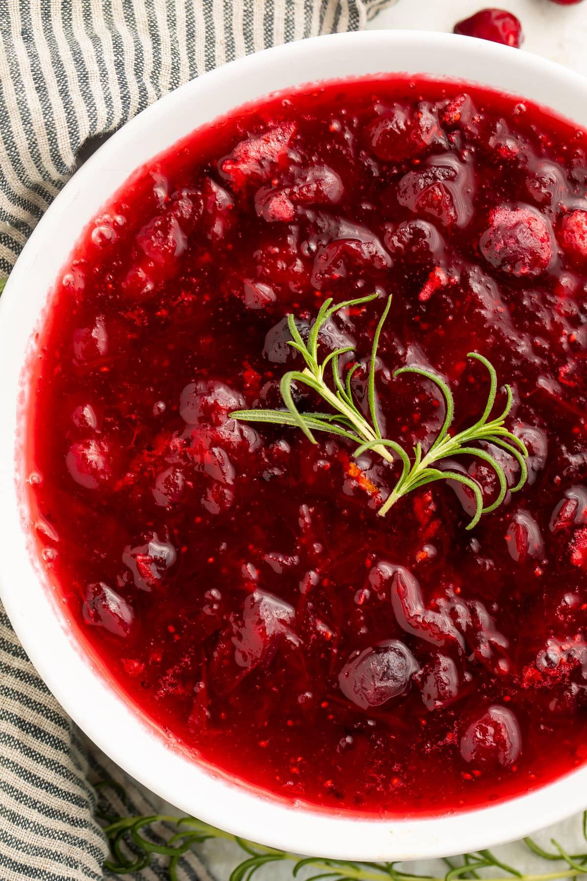 finished cranberry sauce in a serving dish, garnished with fresh orange zest and a sprig of rosemary