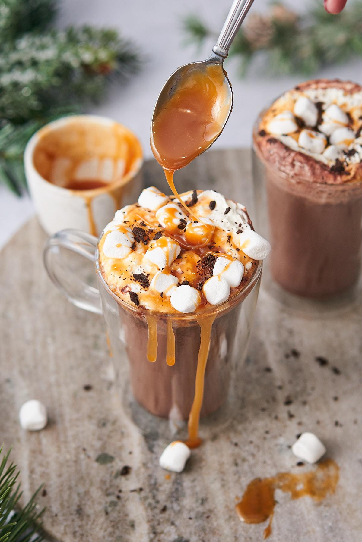 Decadent salted caramel hot chocolate with whipped cream and caramel drizzle, cozy setting, human hands holding mug