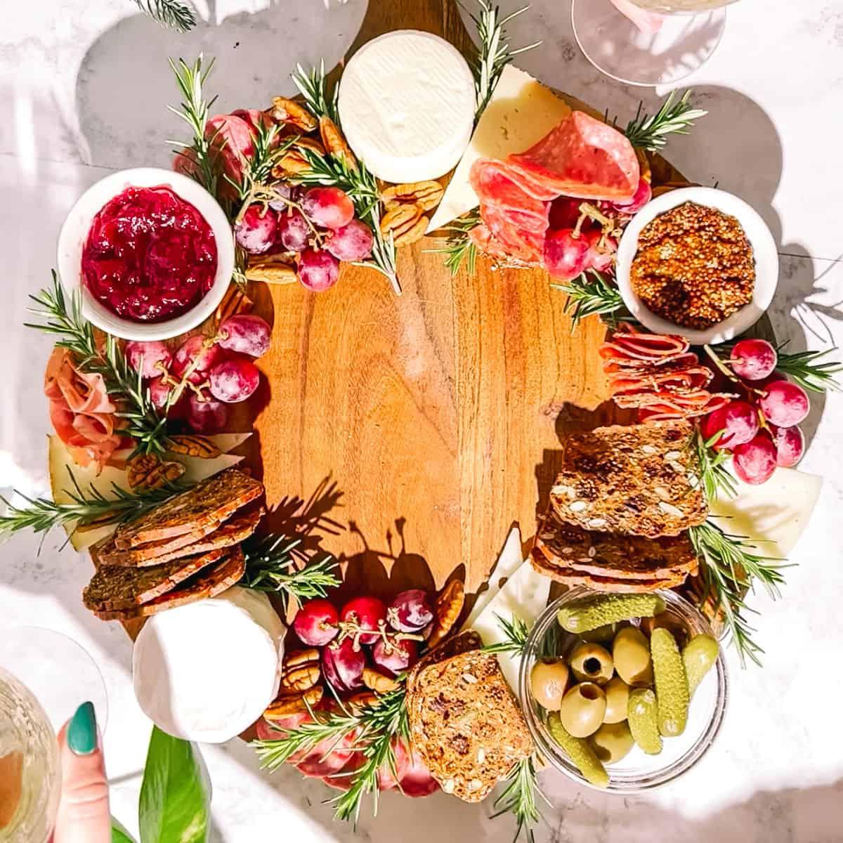 Baked Camembert charcuterie board wreath with various cheeses, cured meats, crackers, fresh fruit, and fig jam on a wooden board