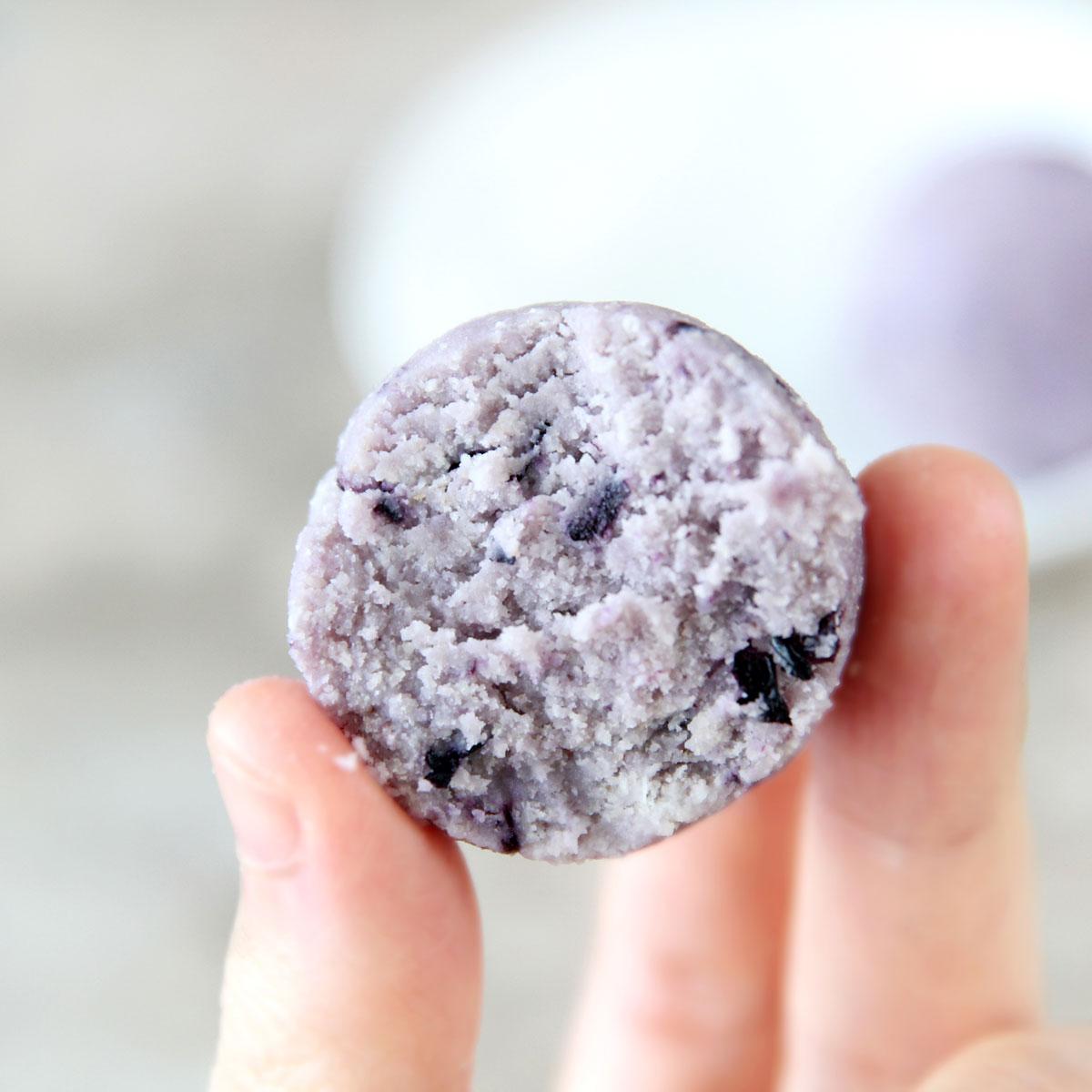 Close up of a hand selecting a low carb blueberry cheesecake bite from a plate.