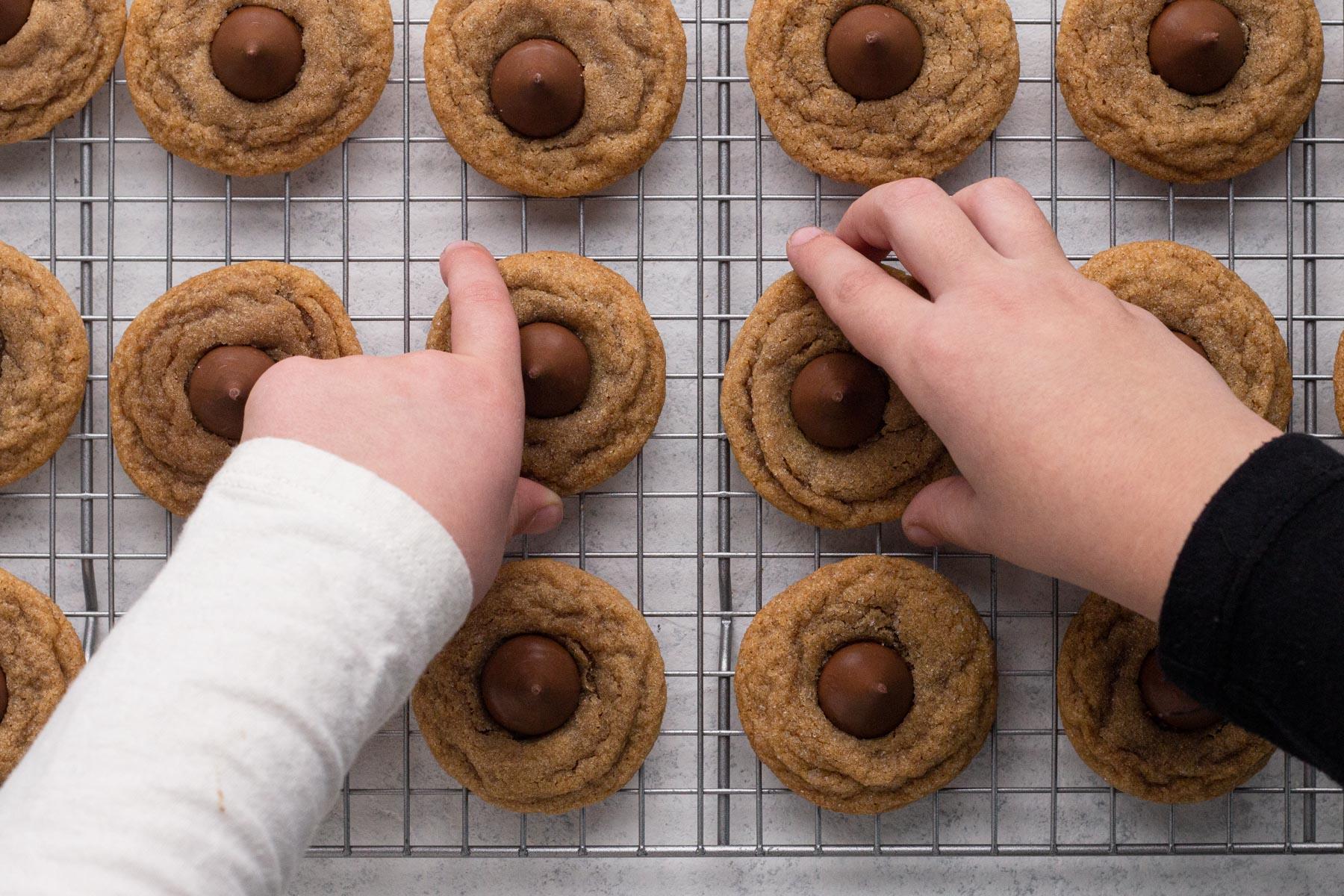 Child's hand reaching for a peanut butter cookie on a cooling rack