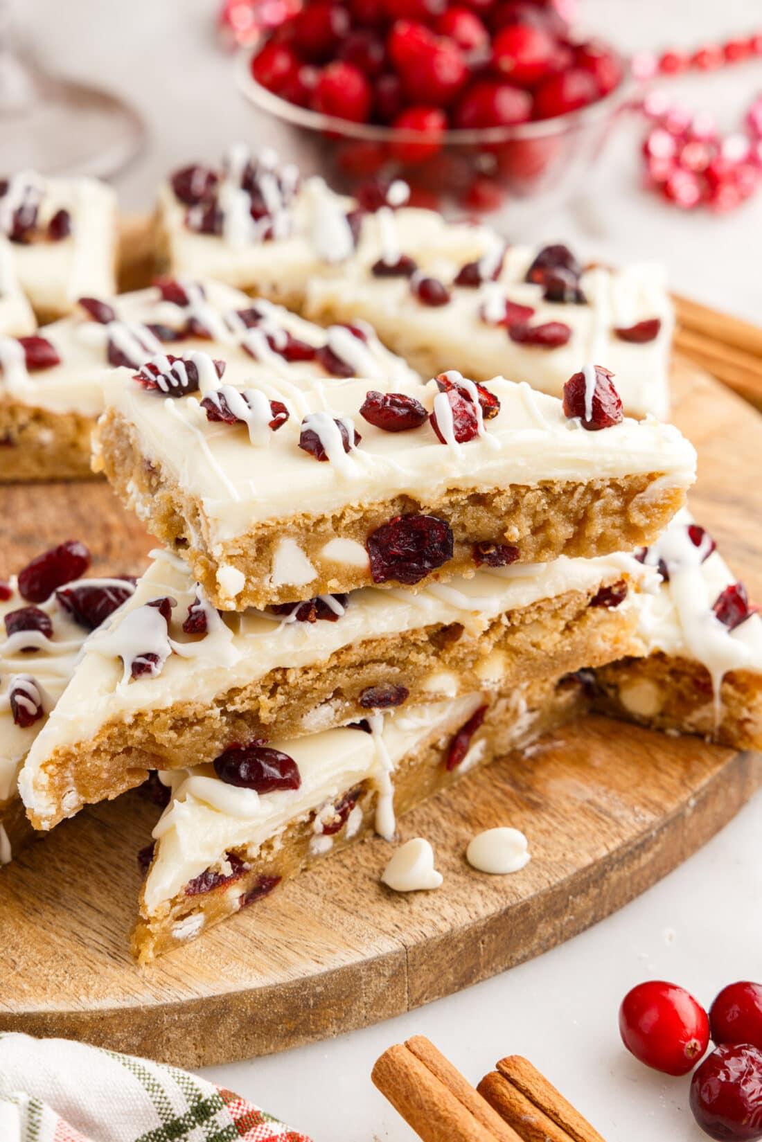 Hands decorating cranberry bliss bars with white chocolate drizzle and orange zest