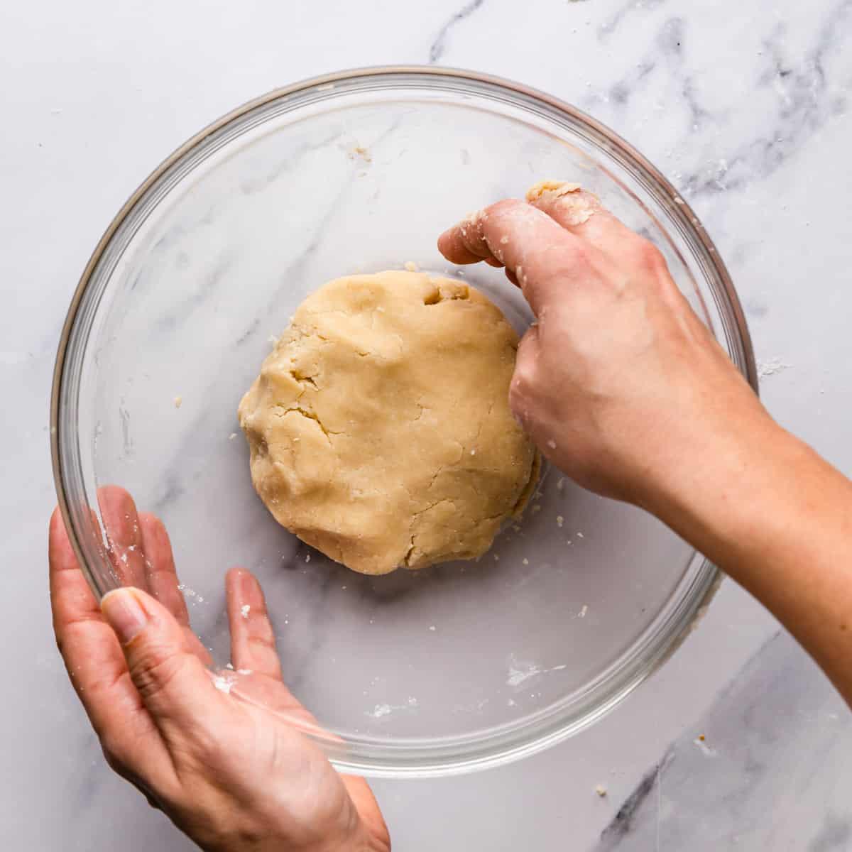 Hands gently kneading espresso shortbread dough on a floured surface, with a rolling pin nearby