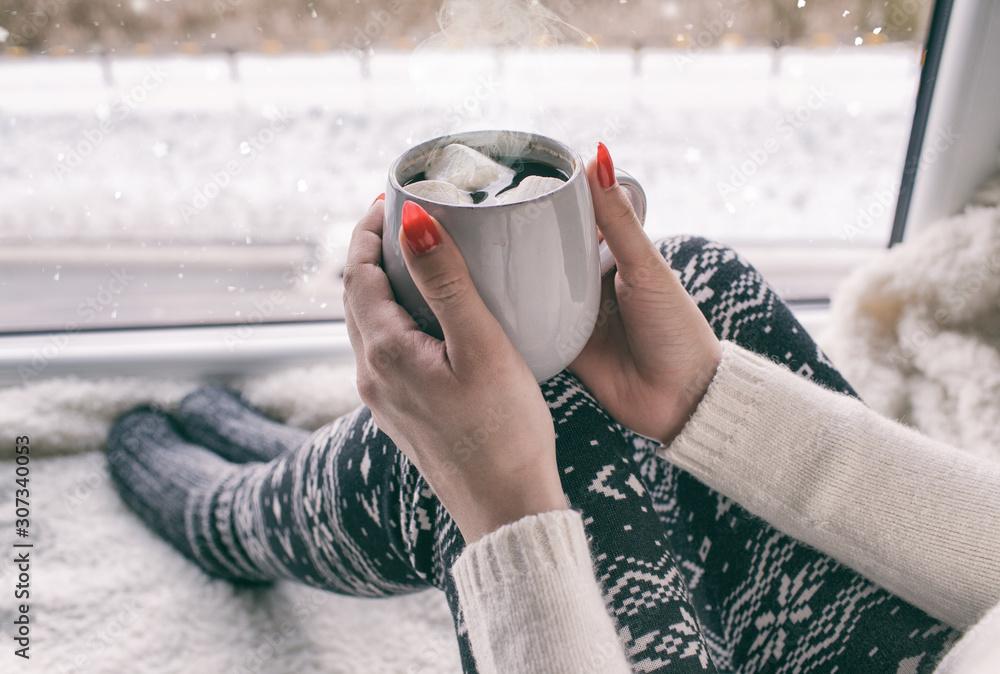person holding a warm mug of mocha hot chocolate by a window on a chilly day