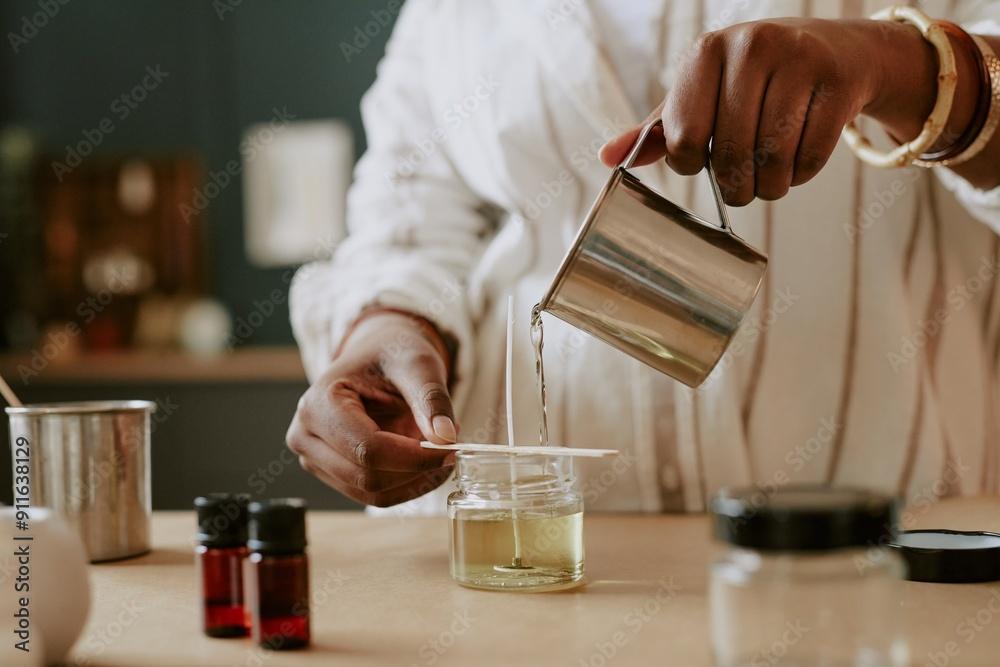 person pouring wax into a candle container