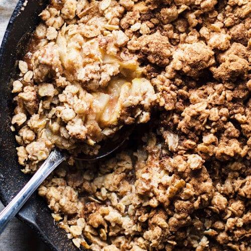 Close-up of a golden-brown apple crumble with cinnamon crust, steam rising, served in a ceramic dish.