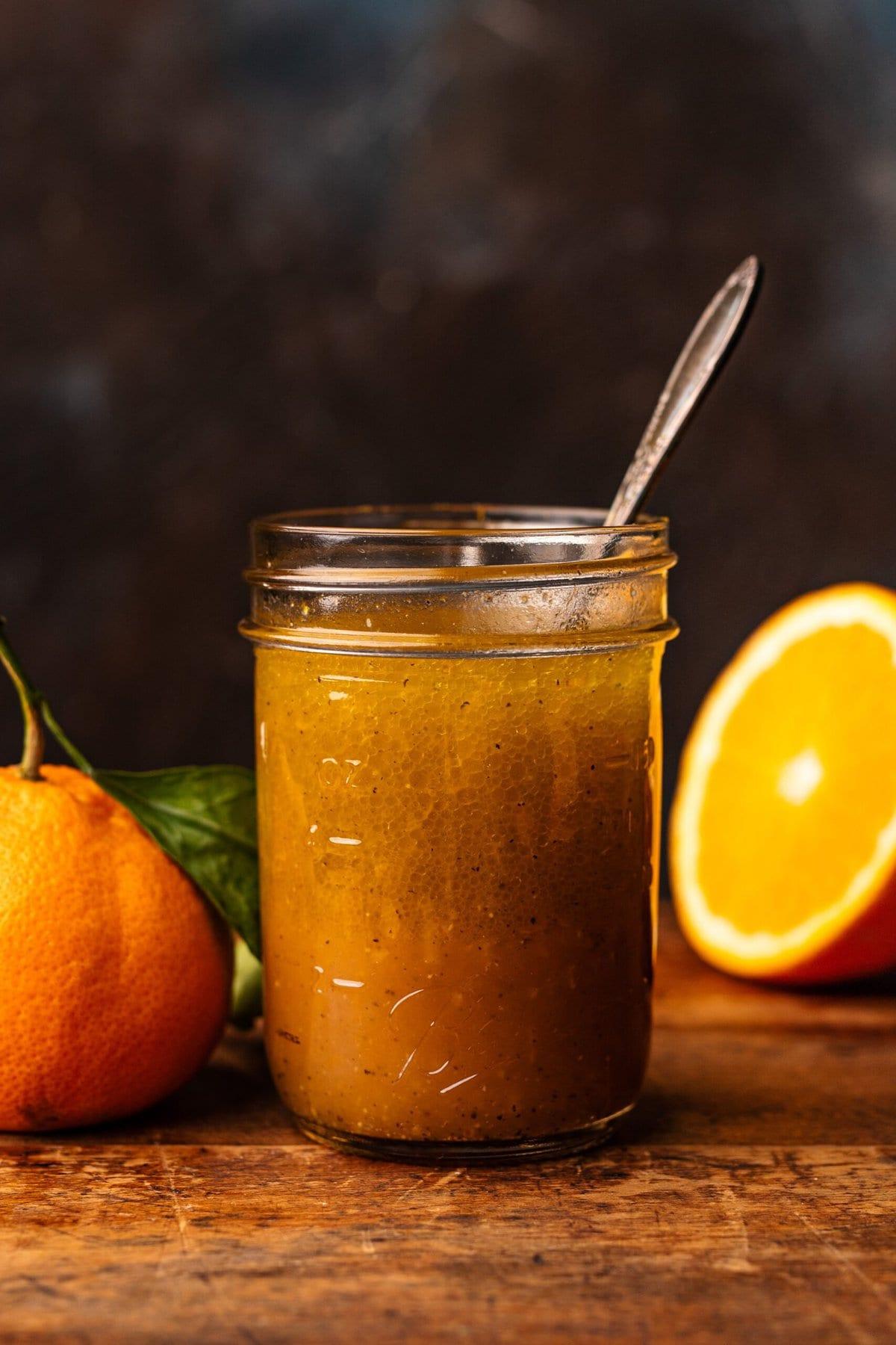 Close-up of freshly made citrus vinaigrette in a clear glass jar with a small whisk beside it