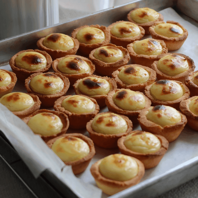 Overhead shot of freshly baked golden mini cheese tarts cooling on a wire rack, garnished with fresh chives