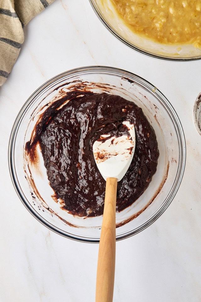 Mixing bowl with banana bread batter, melted dark chocolate being swirled in