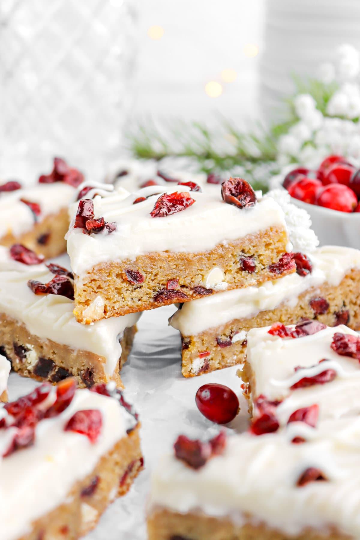 A close-up of a perfectly frosted cranberry bliss bar slice on a white plate, with a fork, ready to be eaten, soft focus background