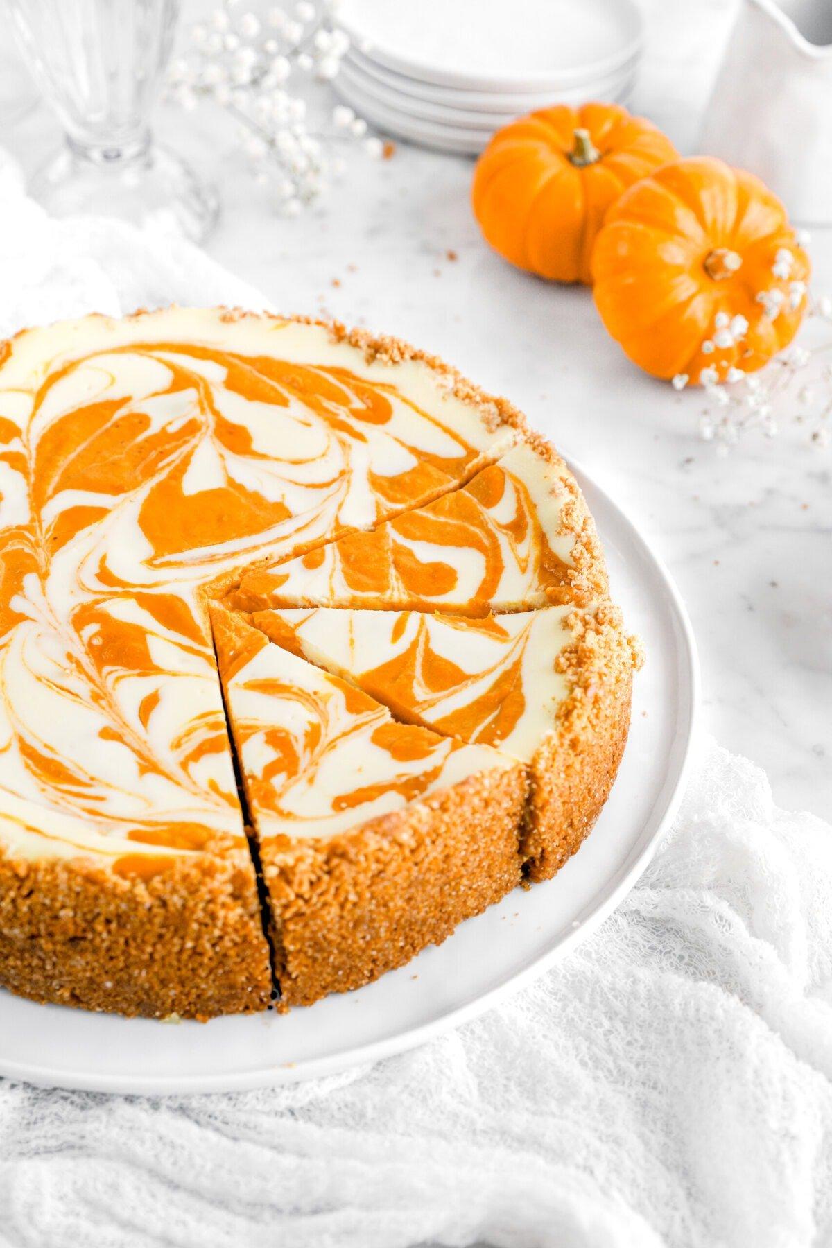 Overhead shot of creamy pumpkin cheesecake with a distinctive white swirl, garnished with fall leaves