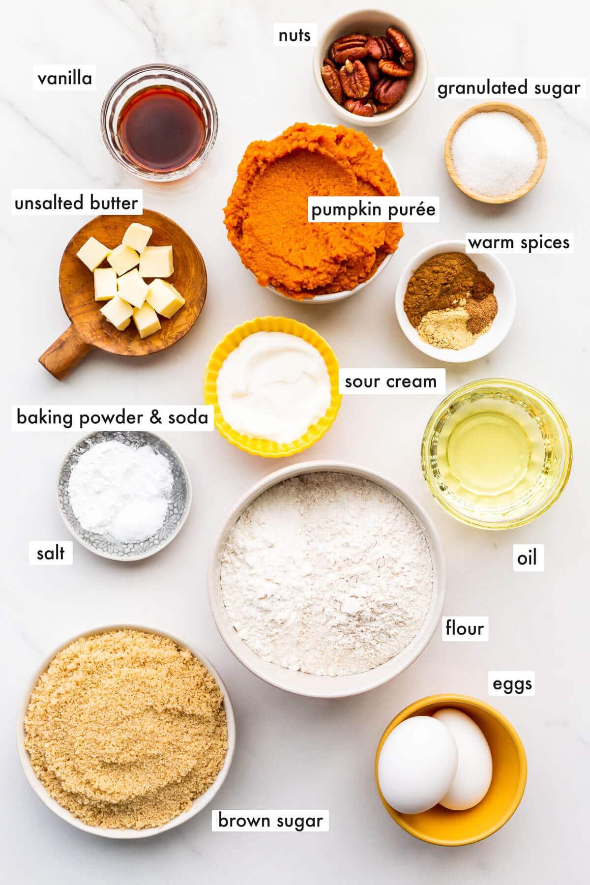 arrangement of ingredients for pumpkin muffins, including pumpkin puree, spices, flour, eggs, and sour cream