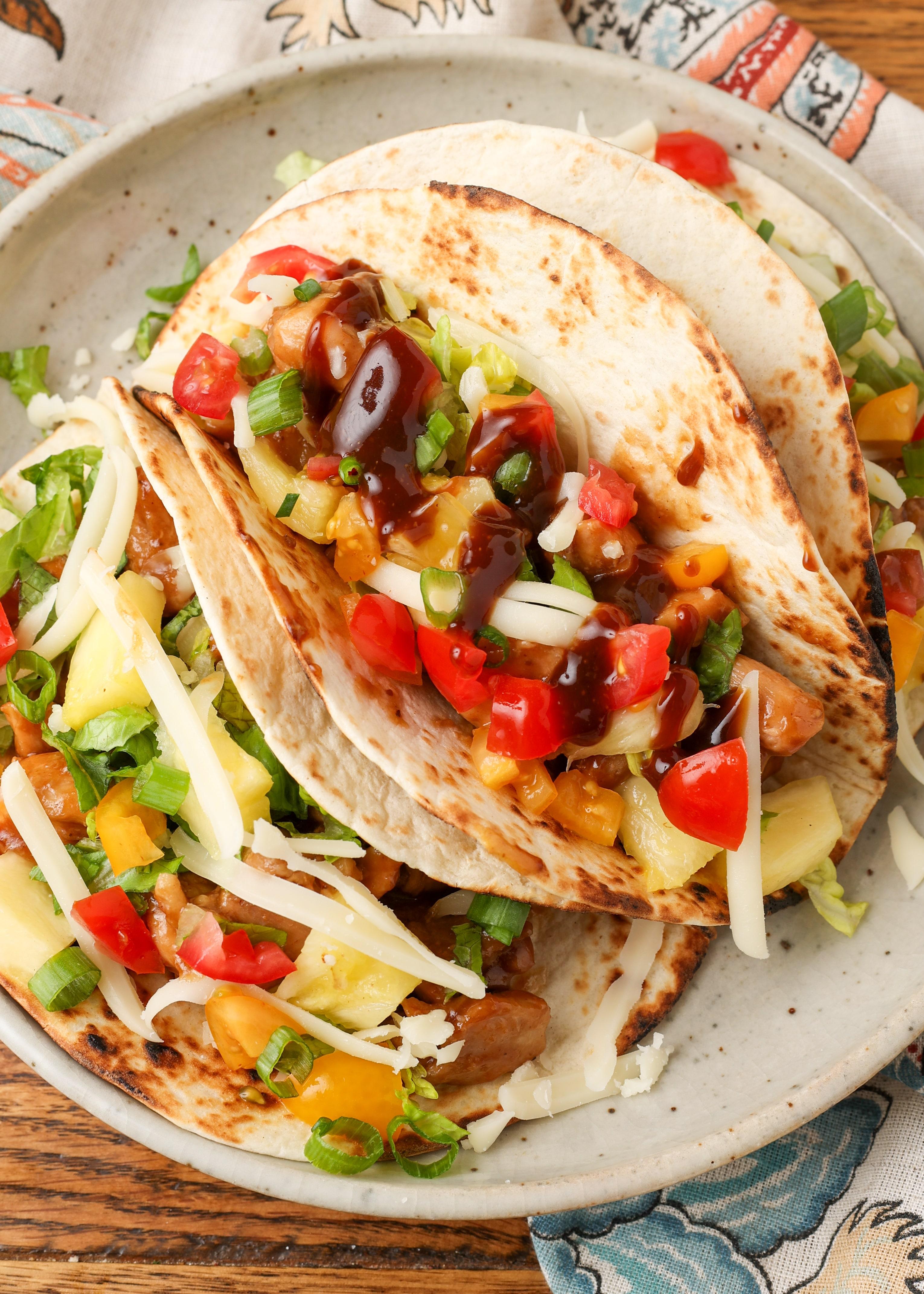 overhead shot of fully assembled pineapple chicken tacos with various toppings