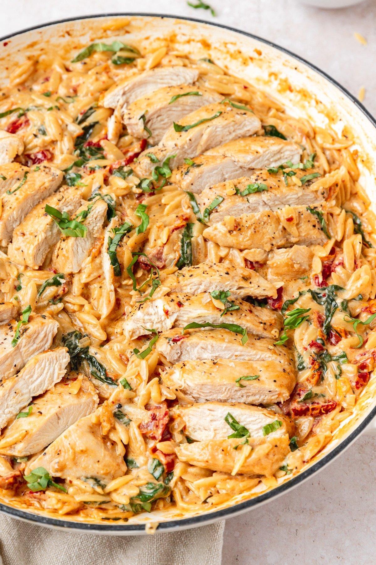 Tuscan chicken orzo pasta dish with creamy sauce, sun-dried tomatoes, and fresh herbs, close-up
