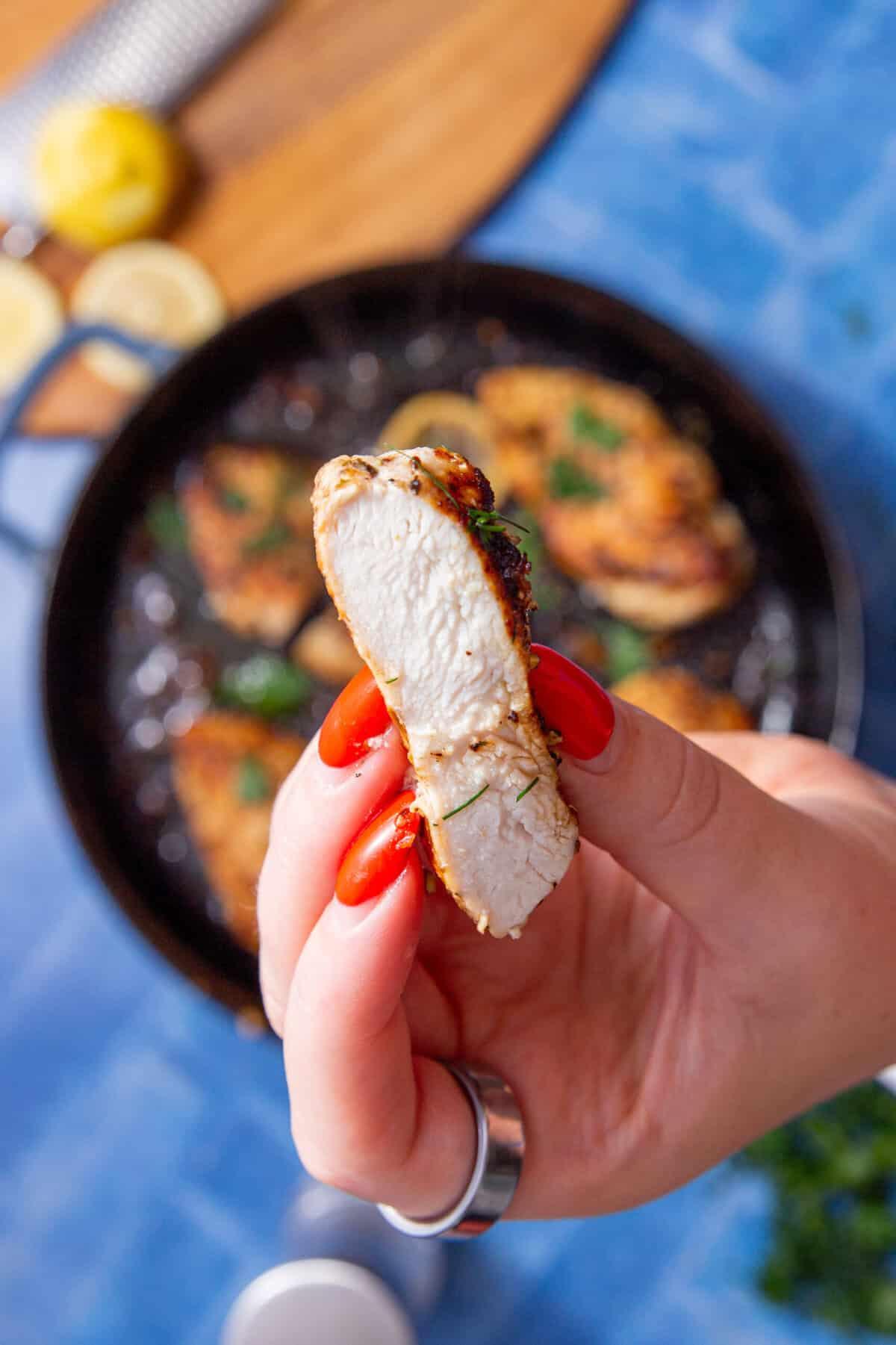 Hand holding a perfectly cooked, sliced chicken breast showing its juicy interior.