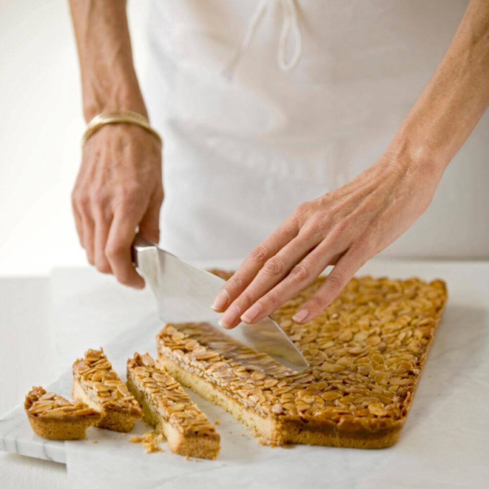 Hands breaking a sheet of golden almond toffee on a cutting board