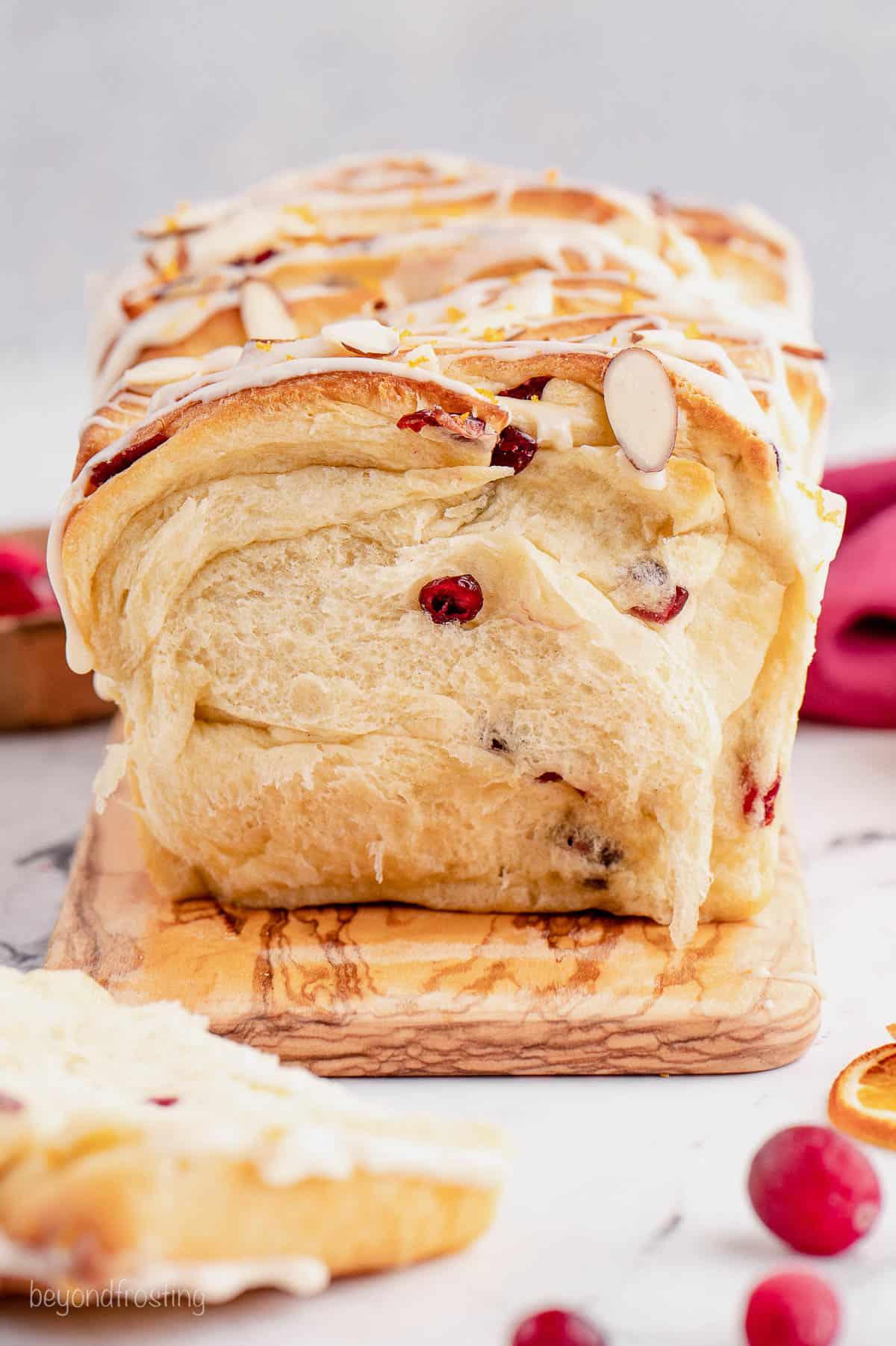 Hand reaching for a slice of cranberry orange bread on a cutting board, with a knife beside it