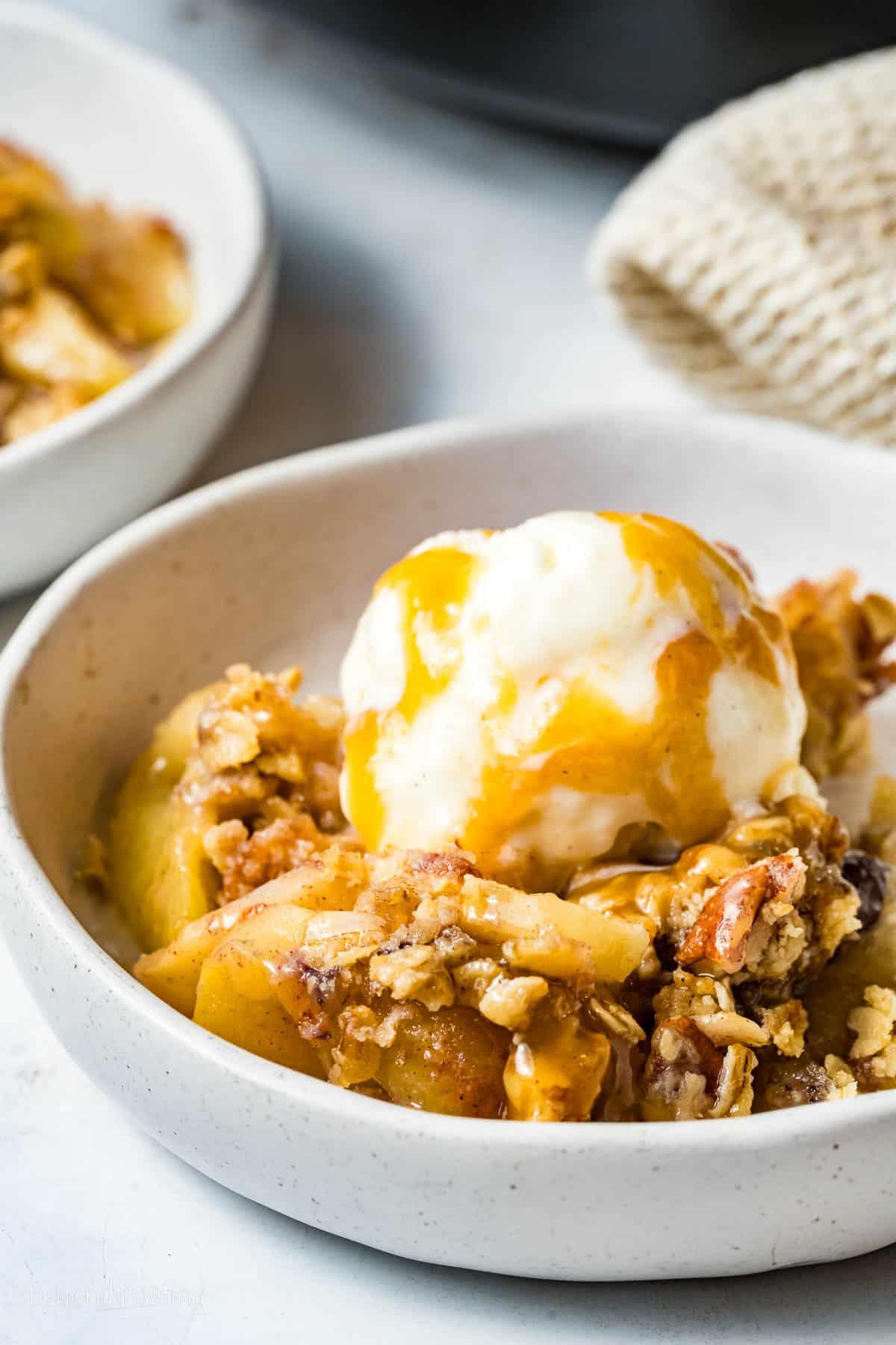 Apple crisp served in a rustic bowl with ice cream and caramel drizzle