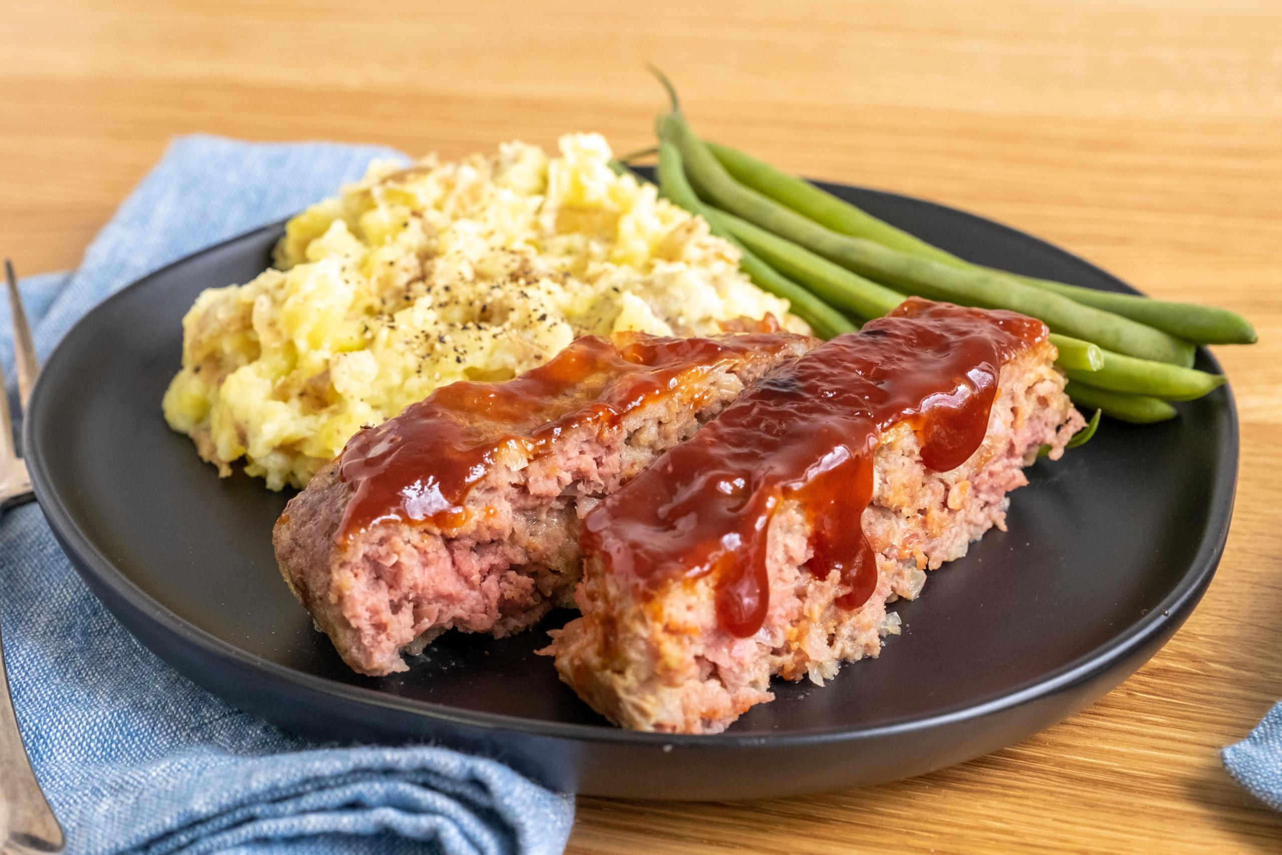 meatloaf sliced on a plate with mashed potatoes and green beans