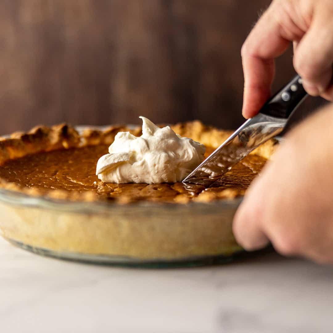hand pouring silky pumpkin pie filling into a pie crust