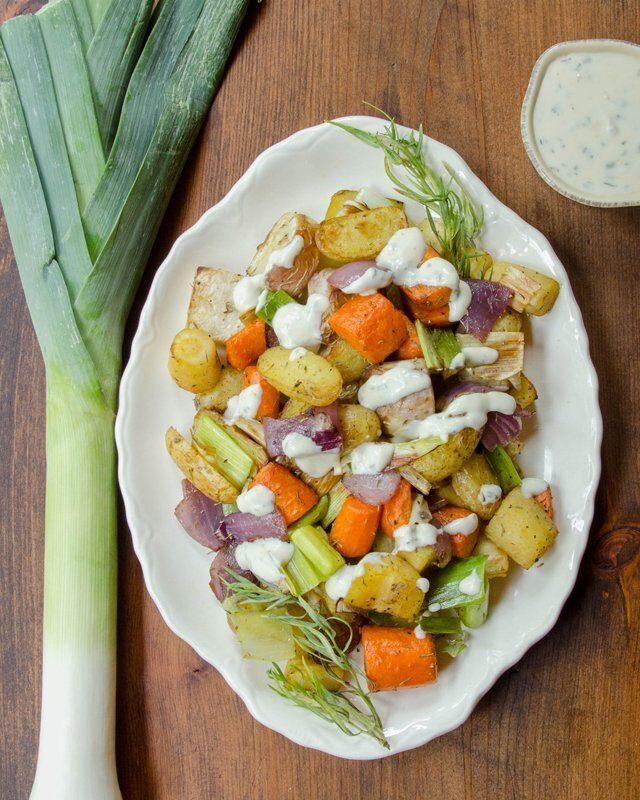 Chef tossing mixed root vegetables with olive oil and dried herbs in a large bowl