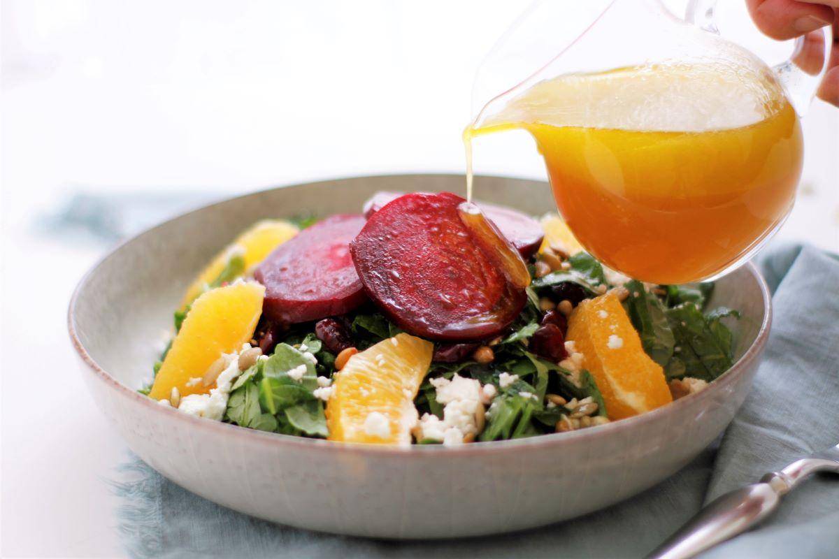Hands drizzling citrus dressing over a roasted beet salad