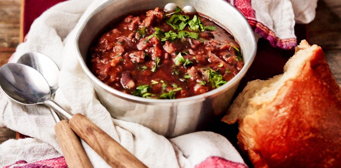 rustic chili stew in a cast iron pot on a wooden table with crusty bread, cozy kitchen scene