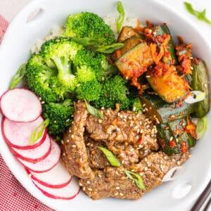 A beautifully plated chili-glazed beef bowl garnished with green onions and sesame seeds and a side of perfectly steamed broccoli, overhead shot