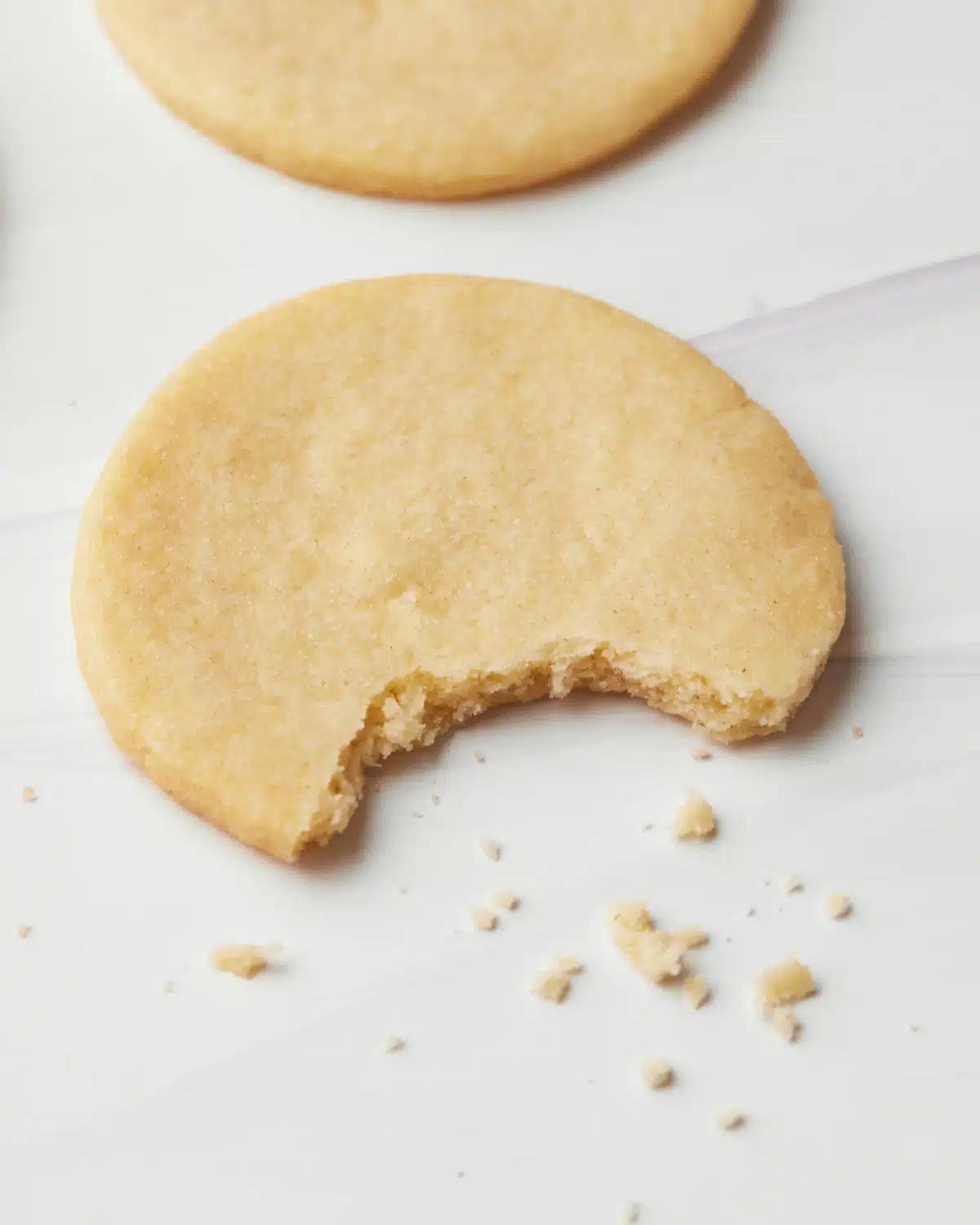 Baked vanilla crumb sugar cookies cooling on a wire rack, with some already taken a bite out of
