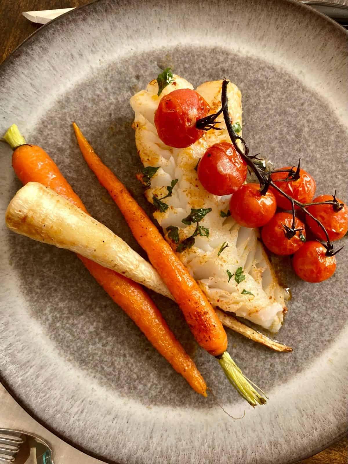 Smiling person plating a dish of baked cod with a side of roasted vegetables.