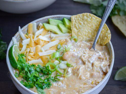 hearty white chicken chili in a rustic bowl with corn chips and cilantro, steamy and inviting, warm lighting, cozy kitchen background