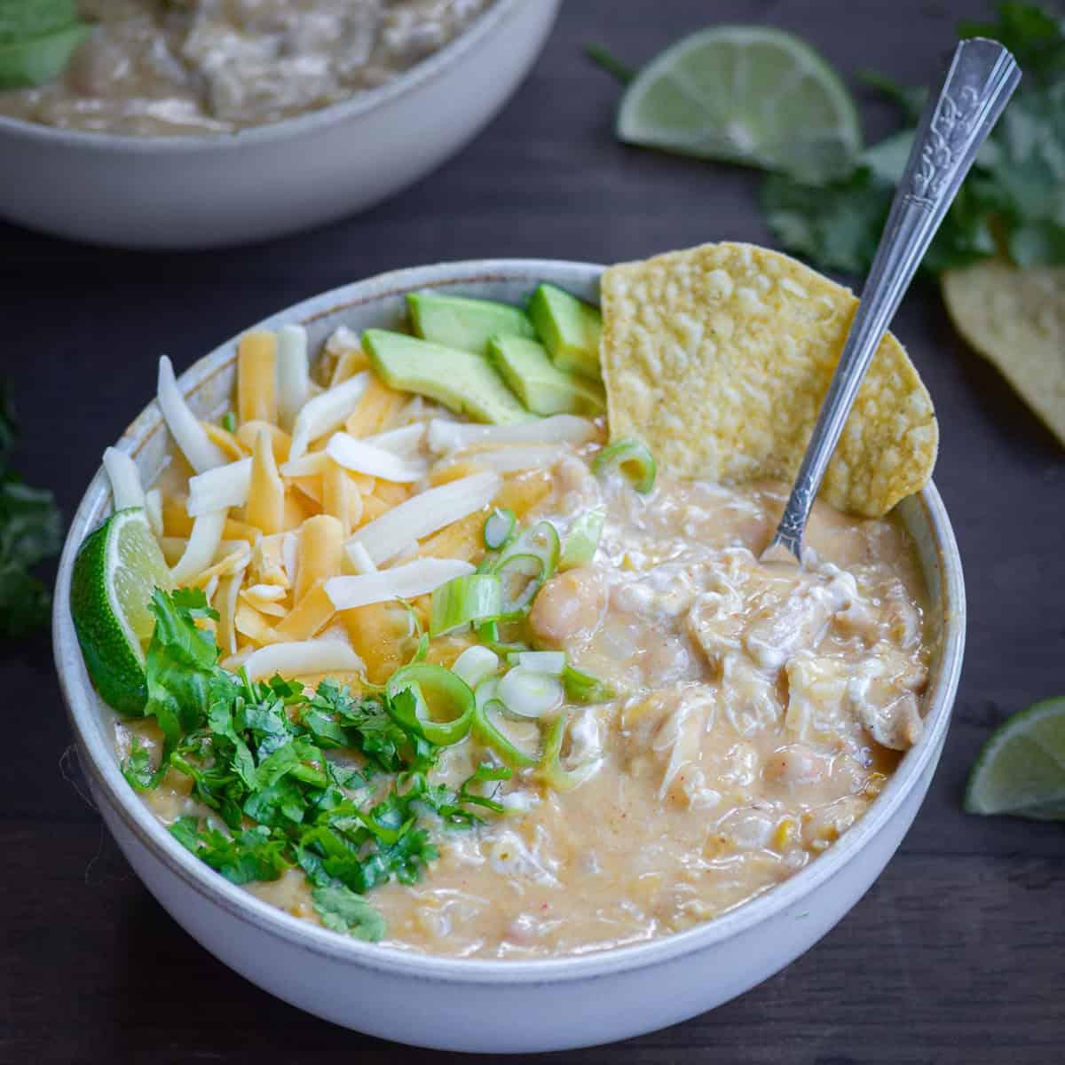 Rustic bowl of creamy white chicken chili with lime and cilantro garnish on a wooden table, cozy setting