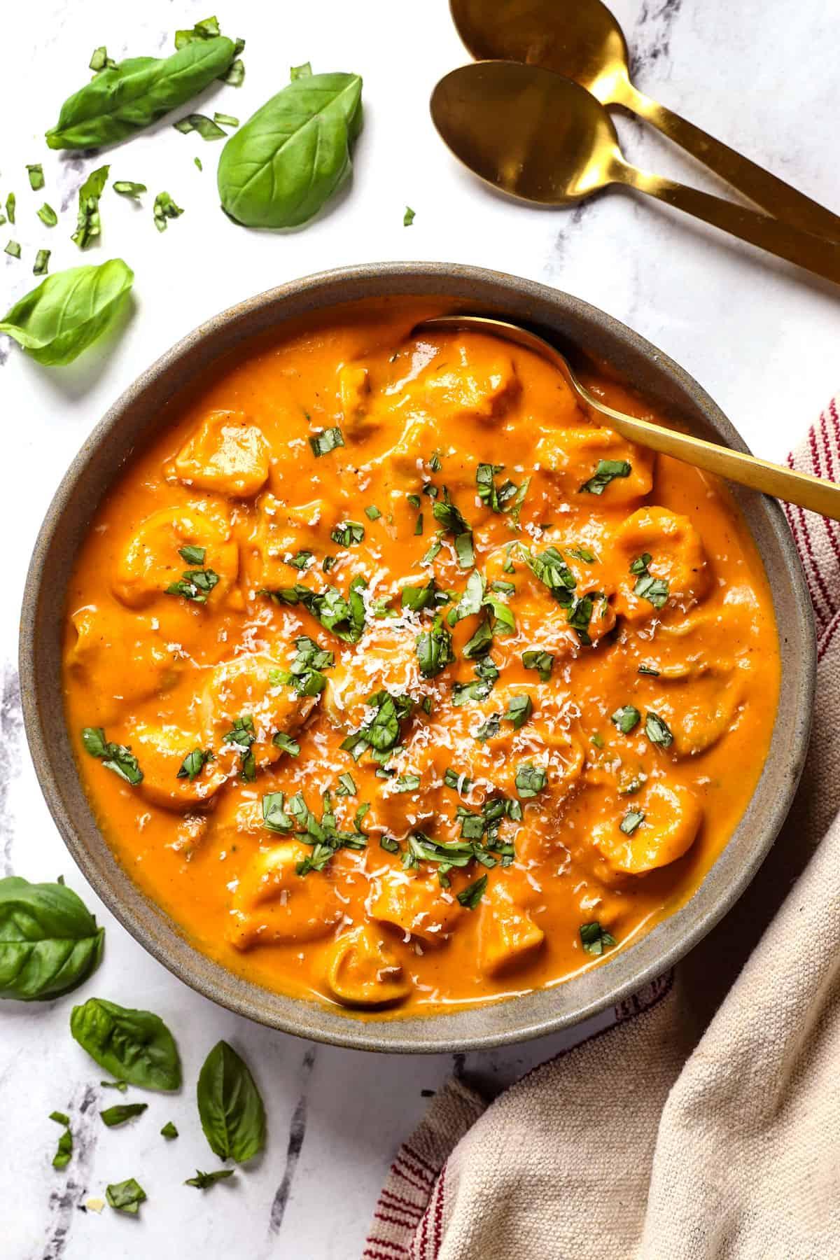 bowl of creamy tomato tortellini soup garnished with basil and parmesan cheese