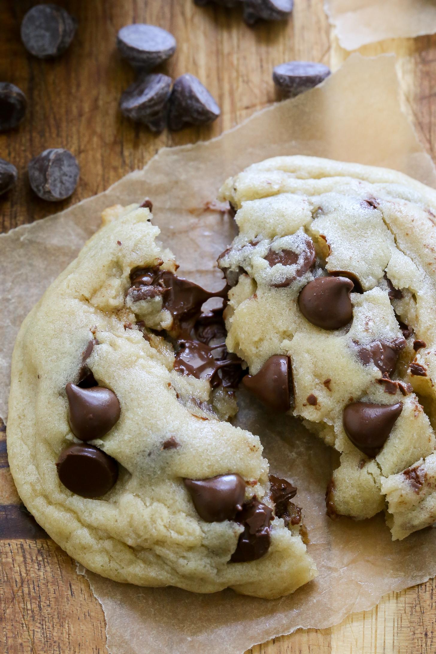 Hands breaking open a warm chocolate chip cookie, showing the gooey, soft center