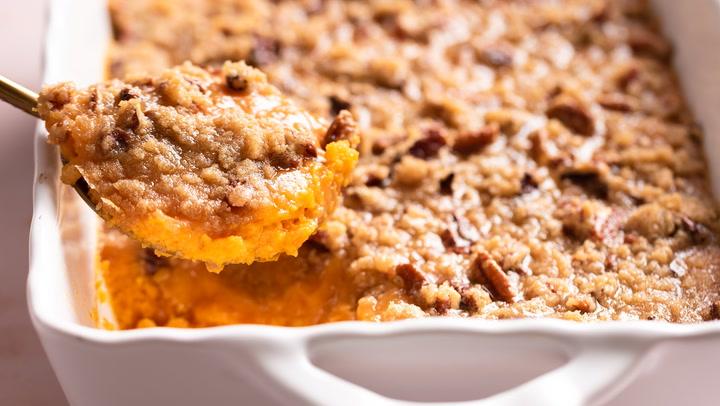 Overhead shot of a full sweet potato casserole dish, golden brown caramelized top, ready to be served, garnished with fresh rosemary and whole pecans.