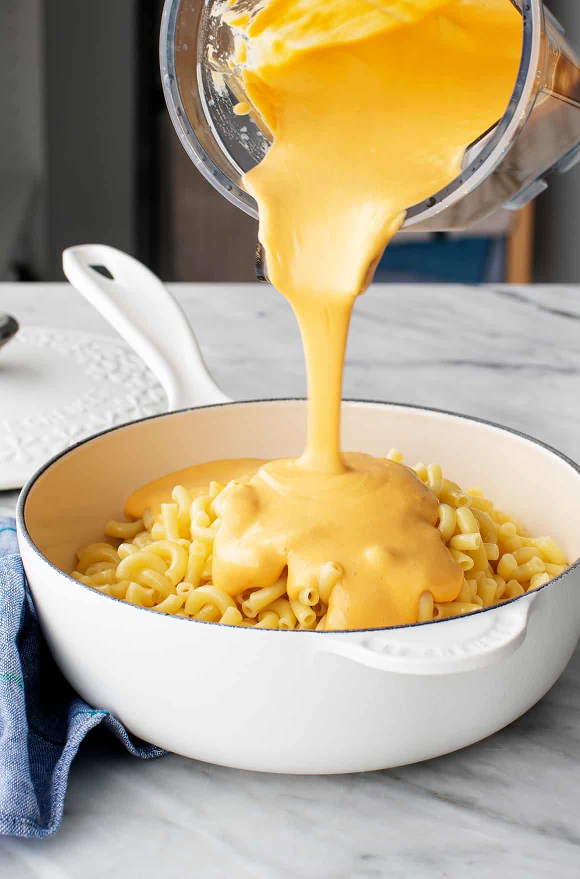 pouring vegan cheese sauce over macaroni noodles