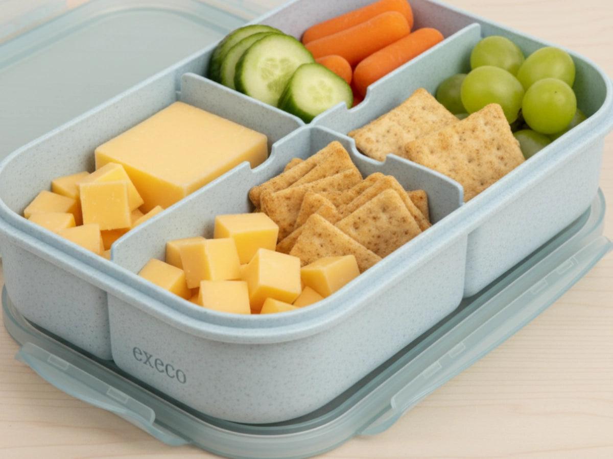 Close-up of various cheeses, crackers, fruits, and nuts in separate compartments of a bento box
