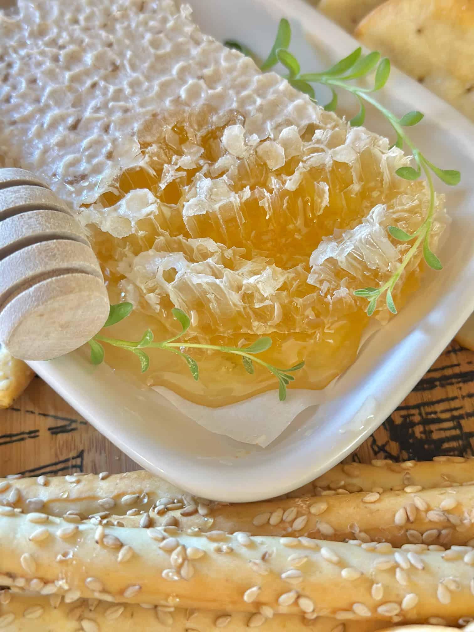 Close-up of a hand reaching for a piece of brie topped with a sliver of honeycomb on a charcuterie board.