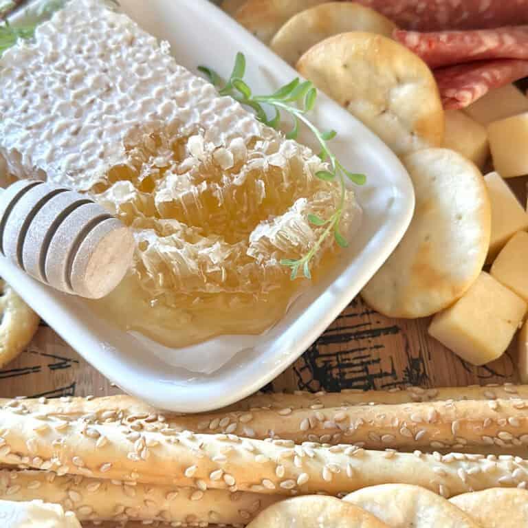 Close-up of a honeycomb piece dripping honey next to a wedge of brie on a charcuterie board.