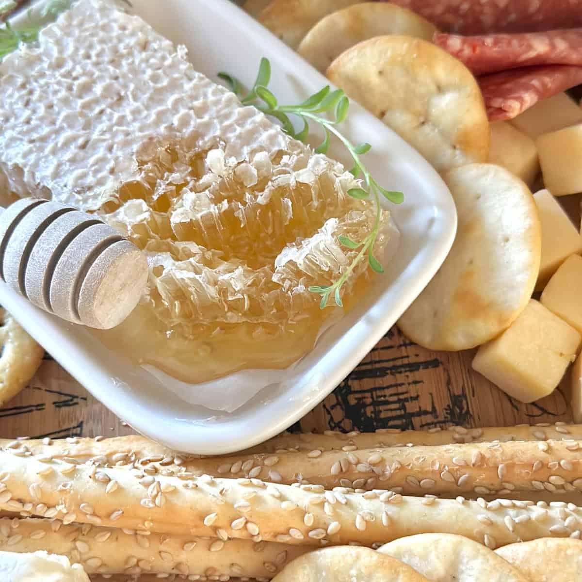 Hands reaching for a piece of brie and honeycomb from a lavishly arranged charcuterie board.