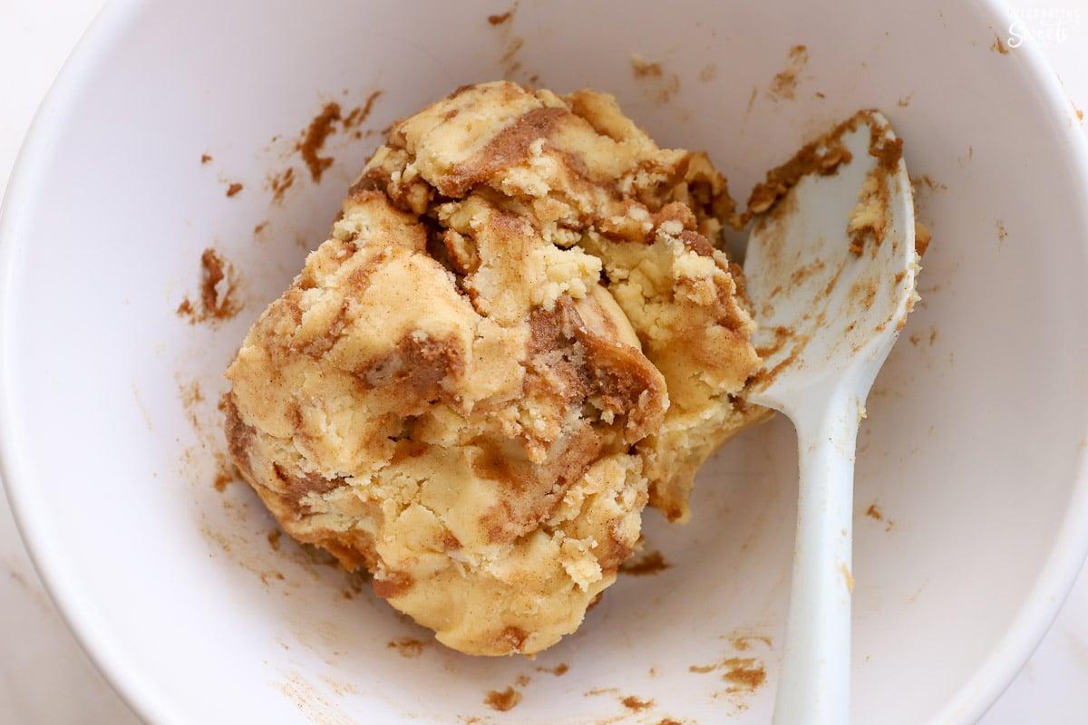 hands rolling cookie dough in a bowl of cinnamon sugar mixture