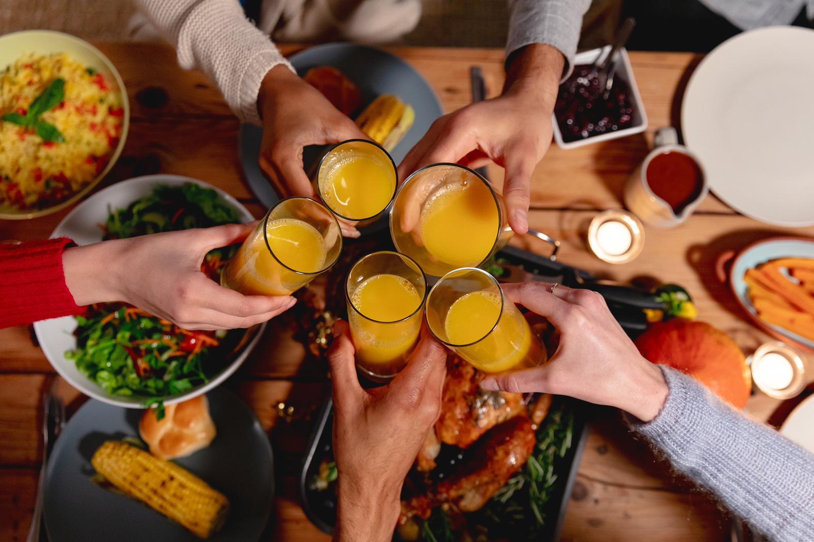 Group of friends laughing and toasting with honey citrus spritz drinks at a Friendsgiving gathering