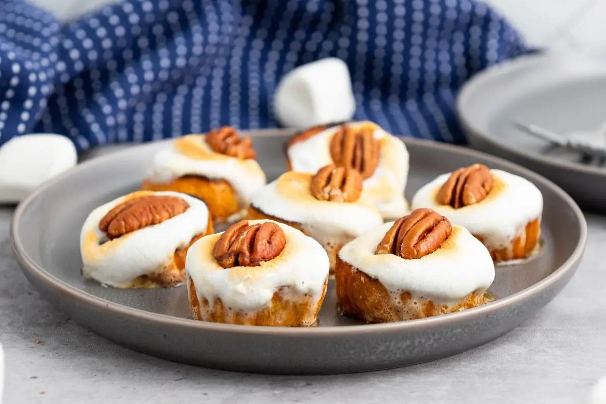 A person, smiling, handing a small plate of glazed sweet potato bites to another person at a casual gathering.