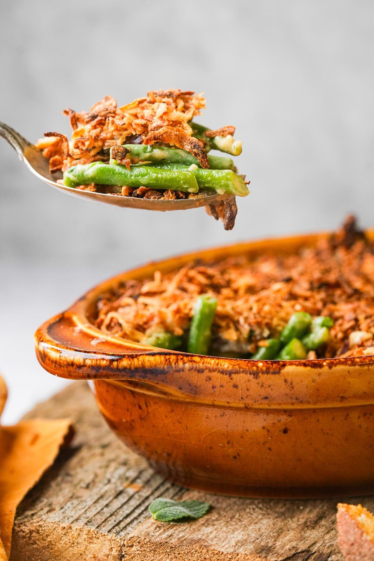 A golden-brown baked green bean casserole with crispy onions and fresh green beans, garnished with parsley, on a rustic wooden table.