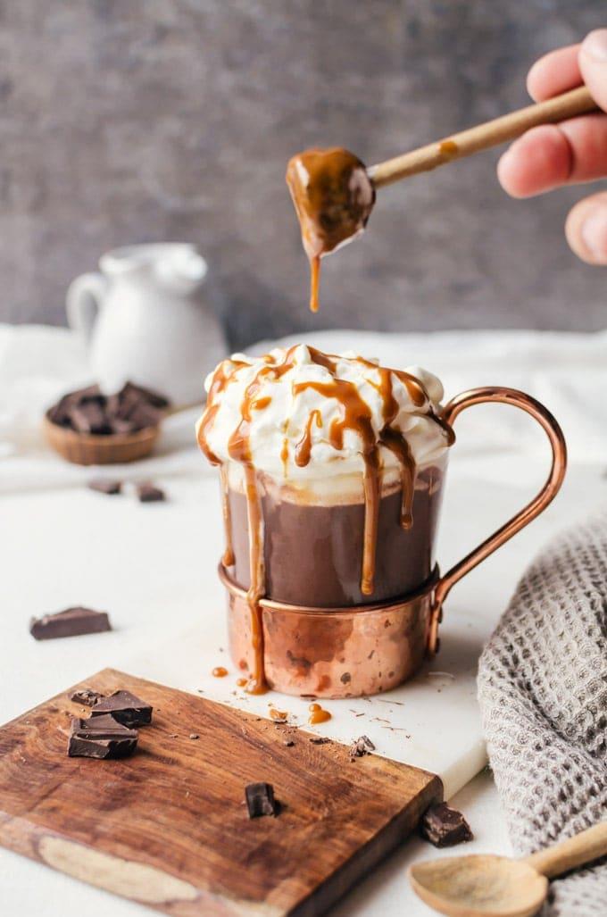 Gourmet spiked hot chocolate with caramel drizzle, whipped cream, and cozy background, shallow depth of field, warm lighting