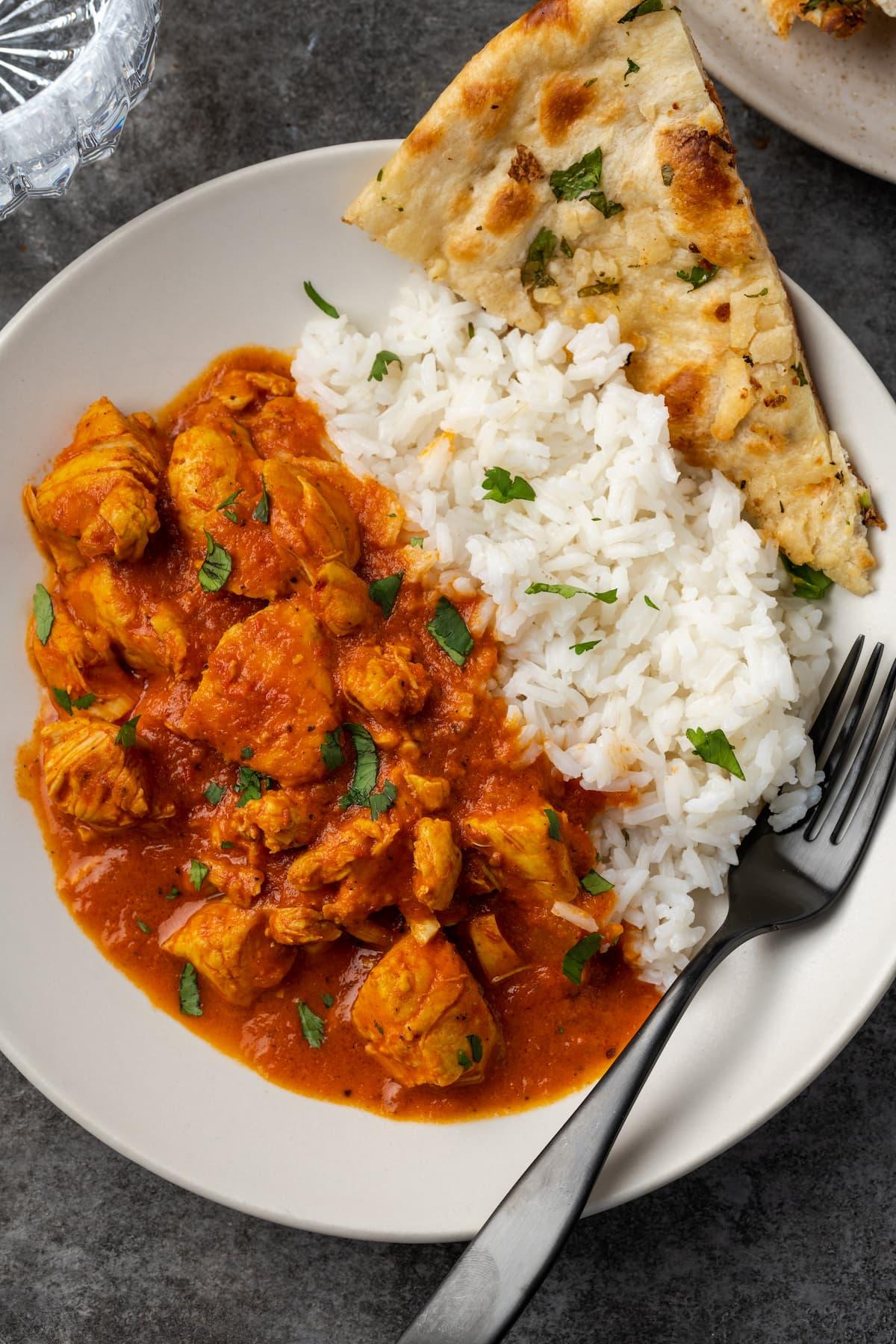 a serving of butter chicken with fluffy basmati rice and garnished with fresh cilantro