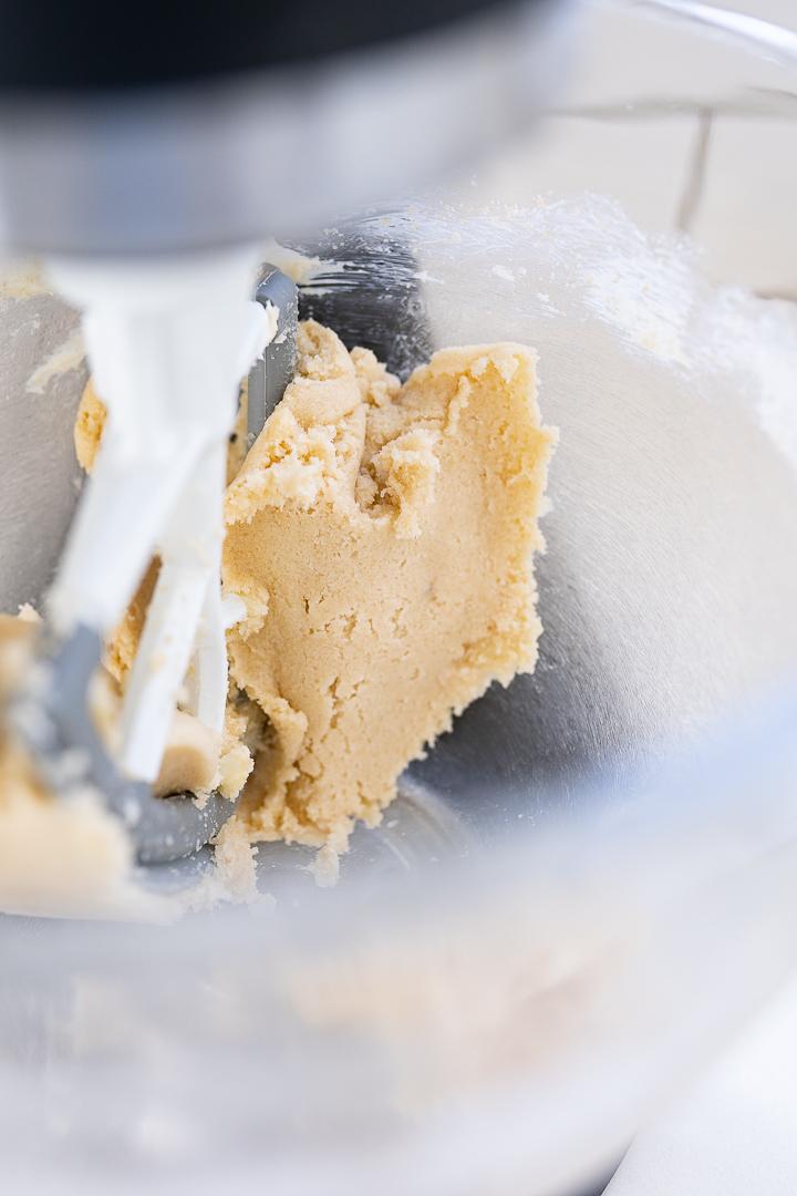 close-up of hands mixing cookie dough in a stand mixer, butter and sugar creaming, soft focus background