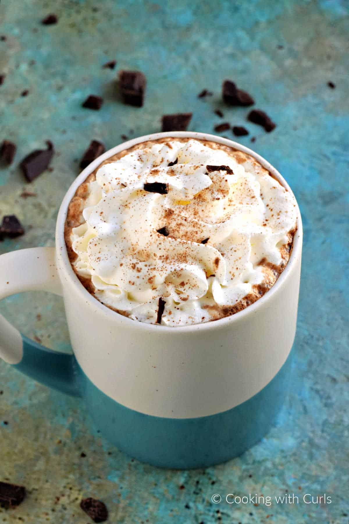 steaming mug of mocha hot chocolate with whipped cream and coffee beans, cozy setting