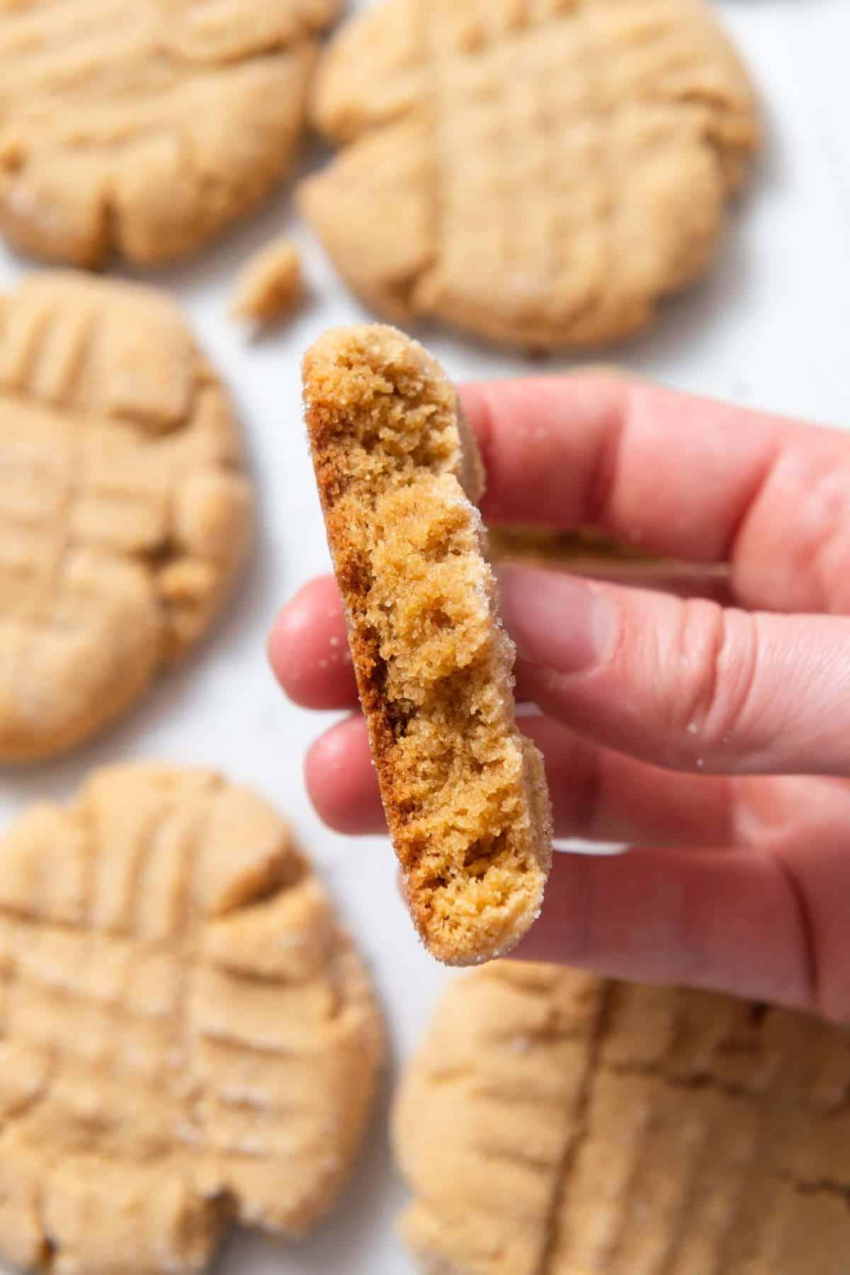 person happily taking a bite out of a peanut butter cookie, showing the soft interior